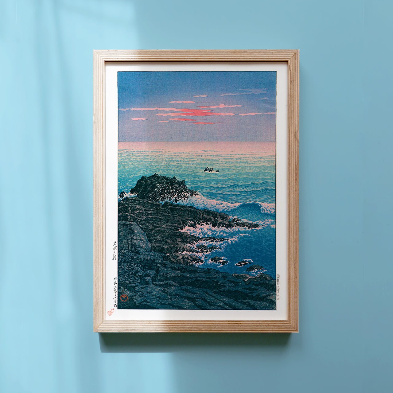 Framed Japanese Art Poster by Kawase Hasui capturing the ocean and rocks at dawn, with pink sky and crashing whitecaps.