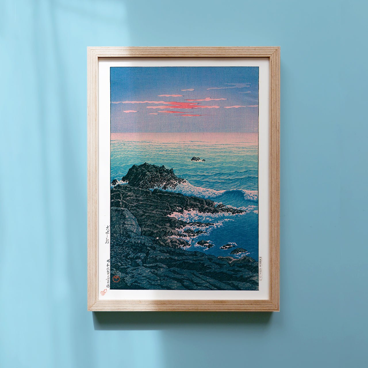 Framed  Japanese Art Poster by Kawase Hasui capturing the ocean and rocks at dawn, with pink sky and crashing whitecaps.